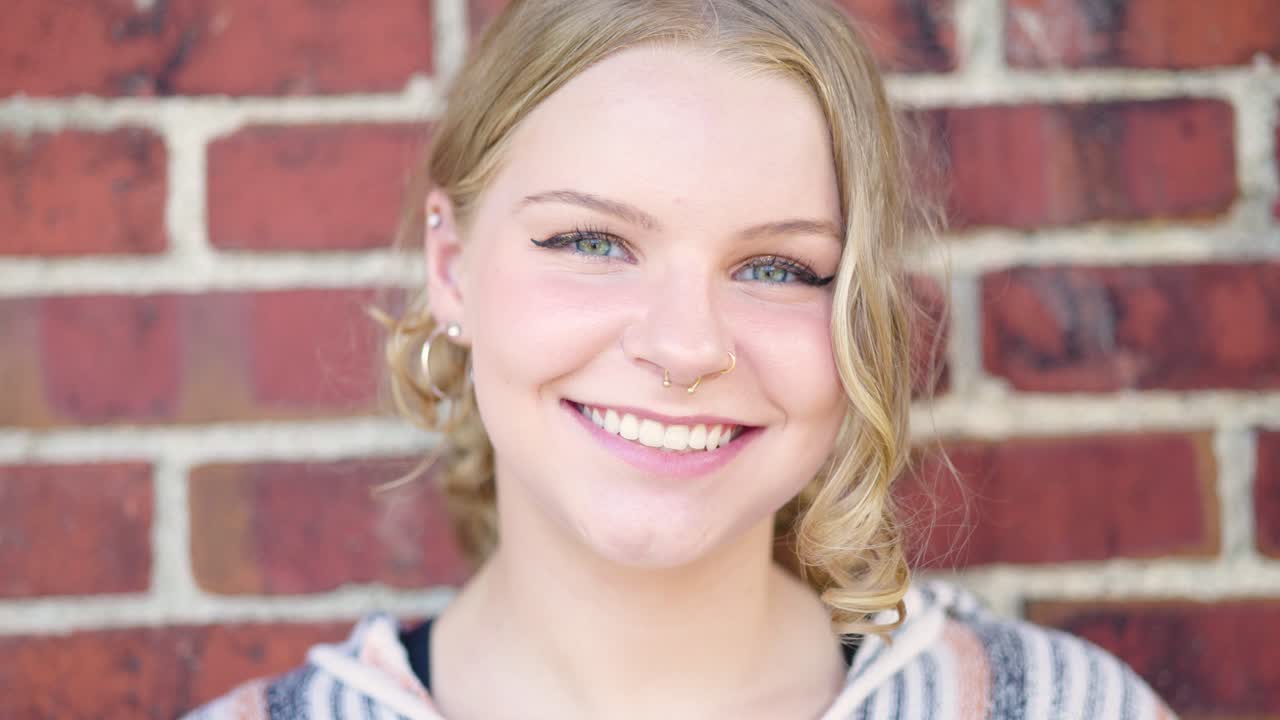 Girl smiling outside against a brick wall