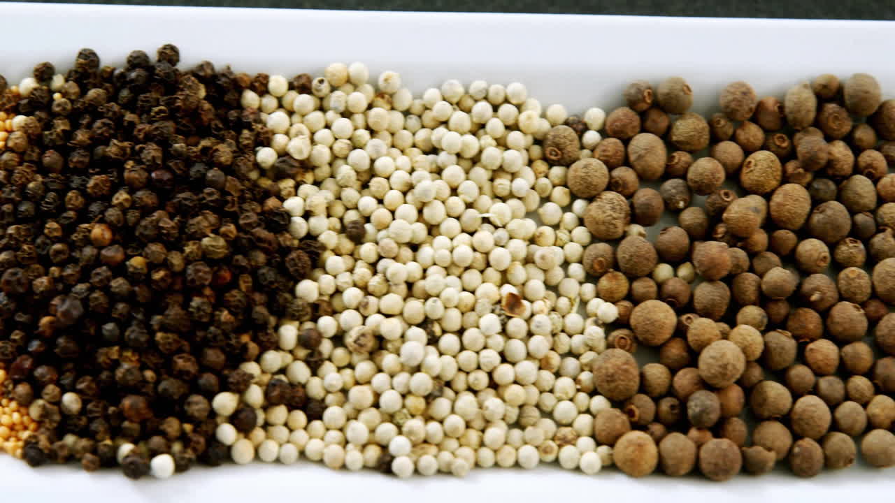 Various spices animation over white rectangular dish with different peppercorns