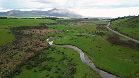 Aerial-4K-epic-view-of-a-large-and-idyllic-green-valley-through-which-a-river-and-a-small-road-pass-in-Mossburn-area