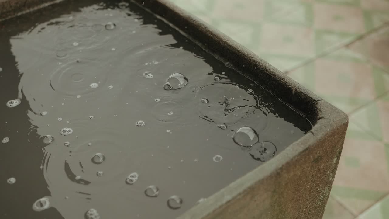 close up of rain falling into a stone basin with ripples and bubbles on a quiet tiled patio
