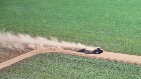 tractor and small road grader turning a bend on a dirt road with dust billowing behind