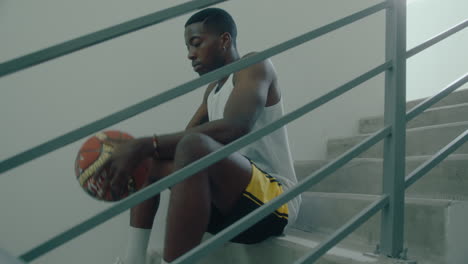 black man sitting on staircase and throwing basketball