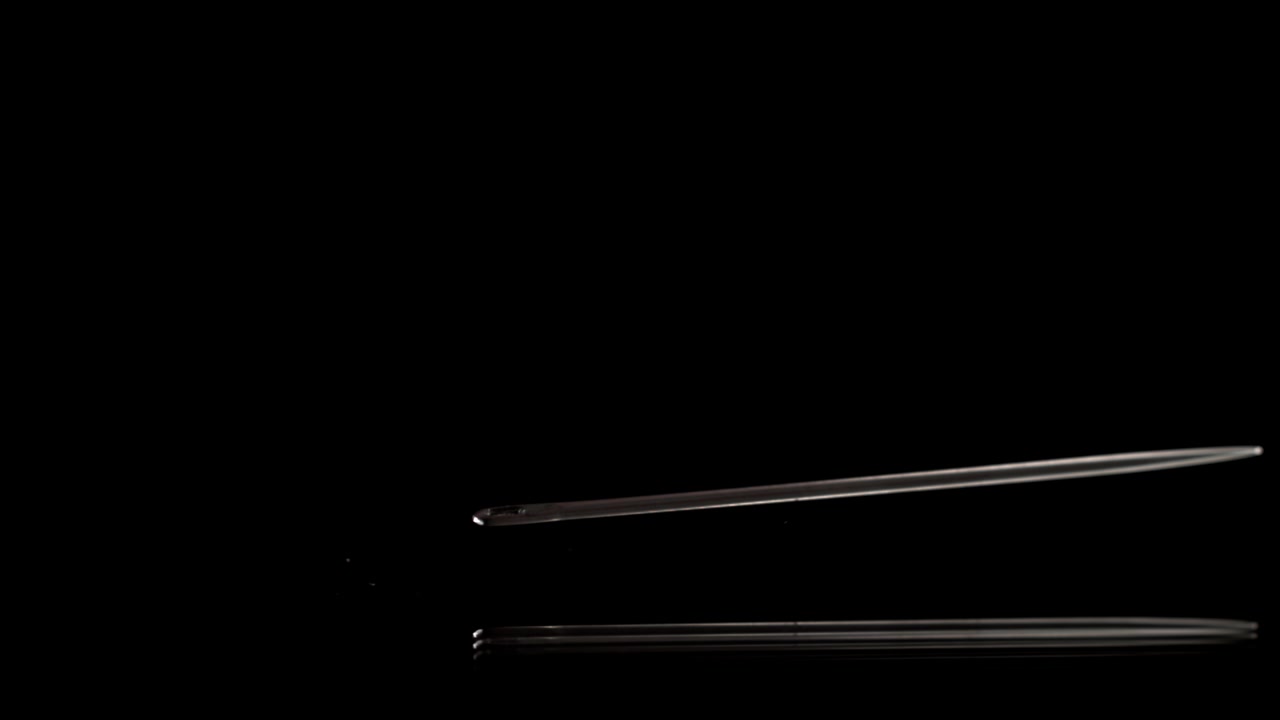 Slow Motion of a Metal Sewing Needle Falling on Black Reflective Surface