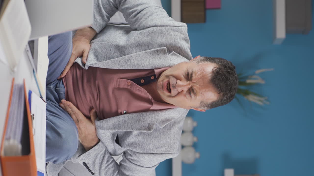 video vertical del trabajador de la oficina en casa el anciano tiene dolor de estómago.