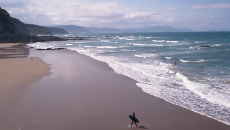 smooth drone view on sopelana beach as a surfer comes out of the water with his board