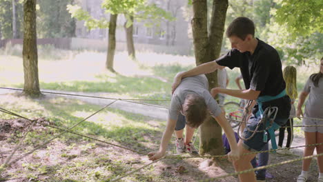 children on a summer camp hike are moving along the ropes with the help of a guide who teaches children rock climbing and tourism. a boy in the forest overcomes a rope barrier