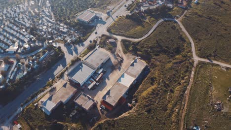aerial view over warehouse beside road near coastline in mitilini, lesbos. follow shot