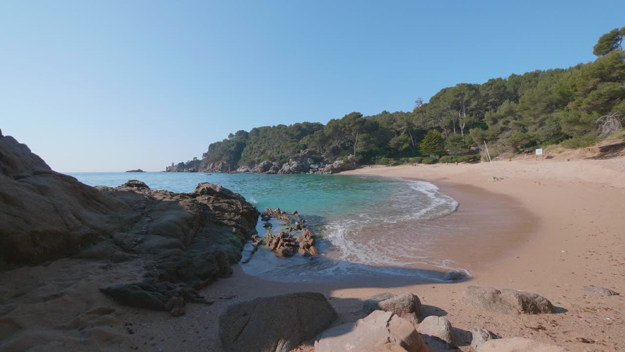 Onde di acqua turchese che si infrangono su una spiaggia di sabbia rosa in Costa Brava, Spagna