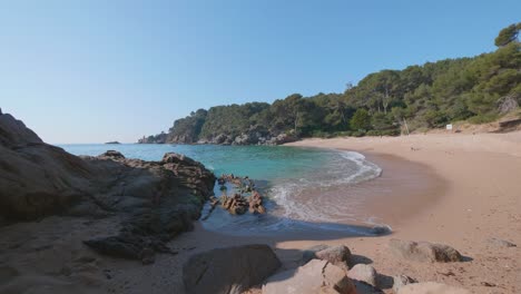 Olas-De-Agua-Turquesa-Rodando-En-Una-Playa-De-Arena-Rosa-En-La-Costa-Brava,-España