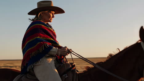 a woman in a cowboy hat riding a horse at sunset