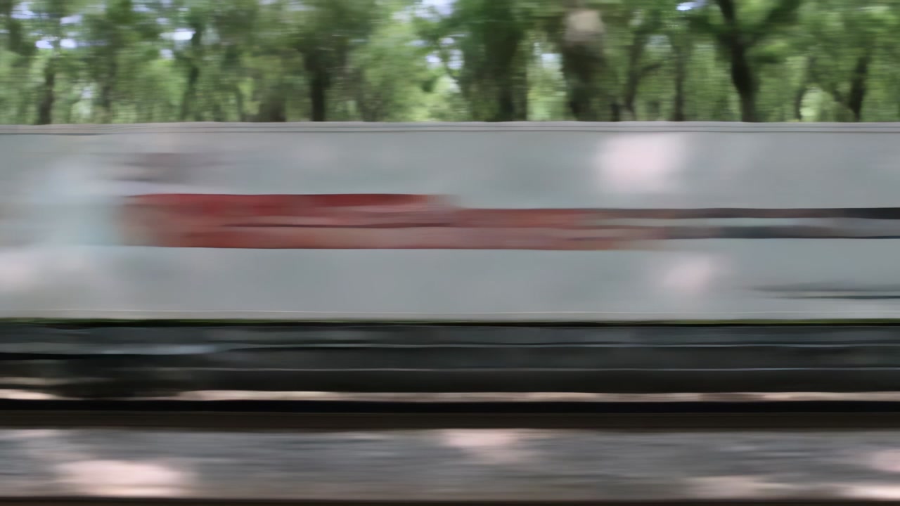 Entering from left, freight train moving right along tree-lined track, hauling freight in box car