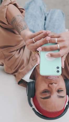 young carefree african american woman lies upside down on sofa and uses phone
