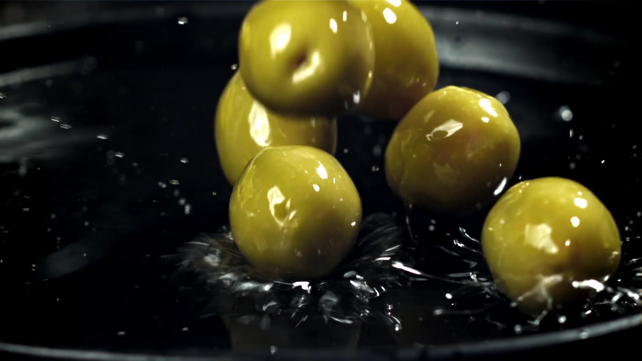 Movimento rallentato di olive verdi che cadono nell'acqua