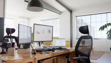 Empty-modern-office-with-graphs-on-computer-screens-and-plants-in-pots-on-tables