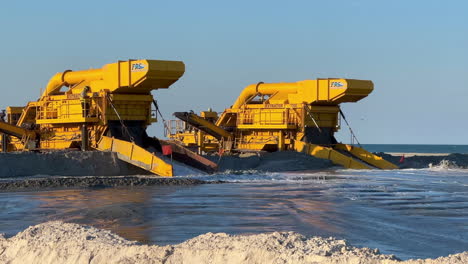 two yellow excavators dredging sand on a beach