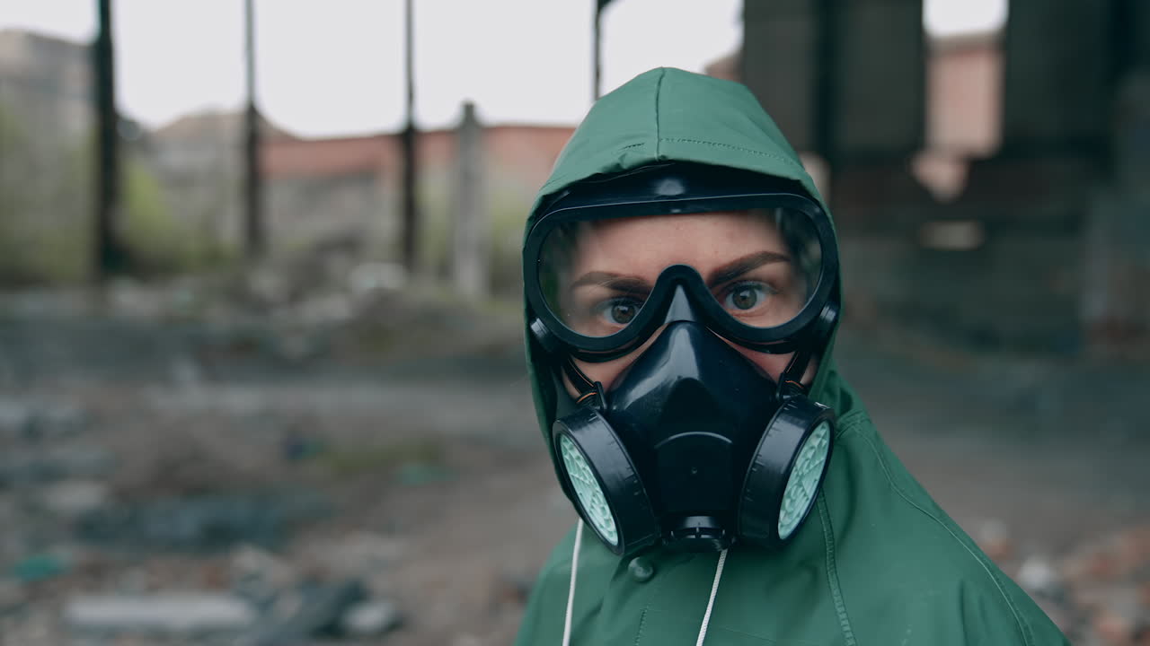 Person in post-apocalyptic place. Survivor in green hazmat suit with gas mask turns his head and looks at camera. Ruined place after chemical attack.