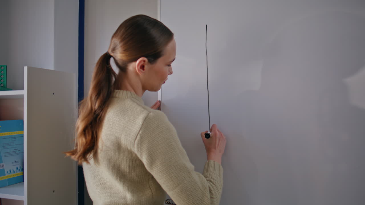 Young professor drawing diagrams whiteboard in classroom closeup. Woman working