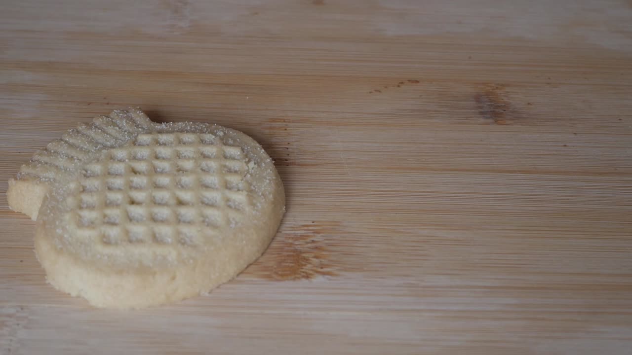 Hand placing shortbread cookies one by one on wooden board, sugar texture visible on the surface