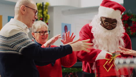 clientes que participan en el sorteo de navidad sostenido por el asistente de venta al por menor vestido de papá noel en una tienda de ropa ornamentada festiva.