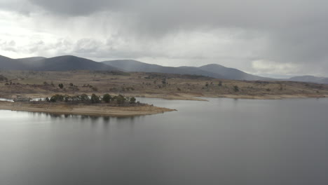 Drone-shot-of-the-shoreline-and-distant-mountains-around-Lake-Jindabyne-on-an-overcast-winters-day