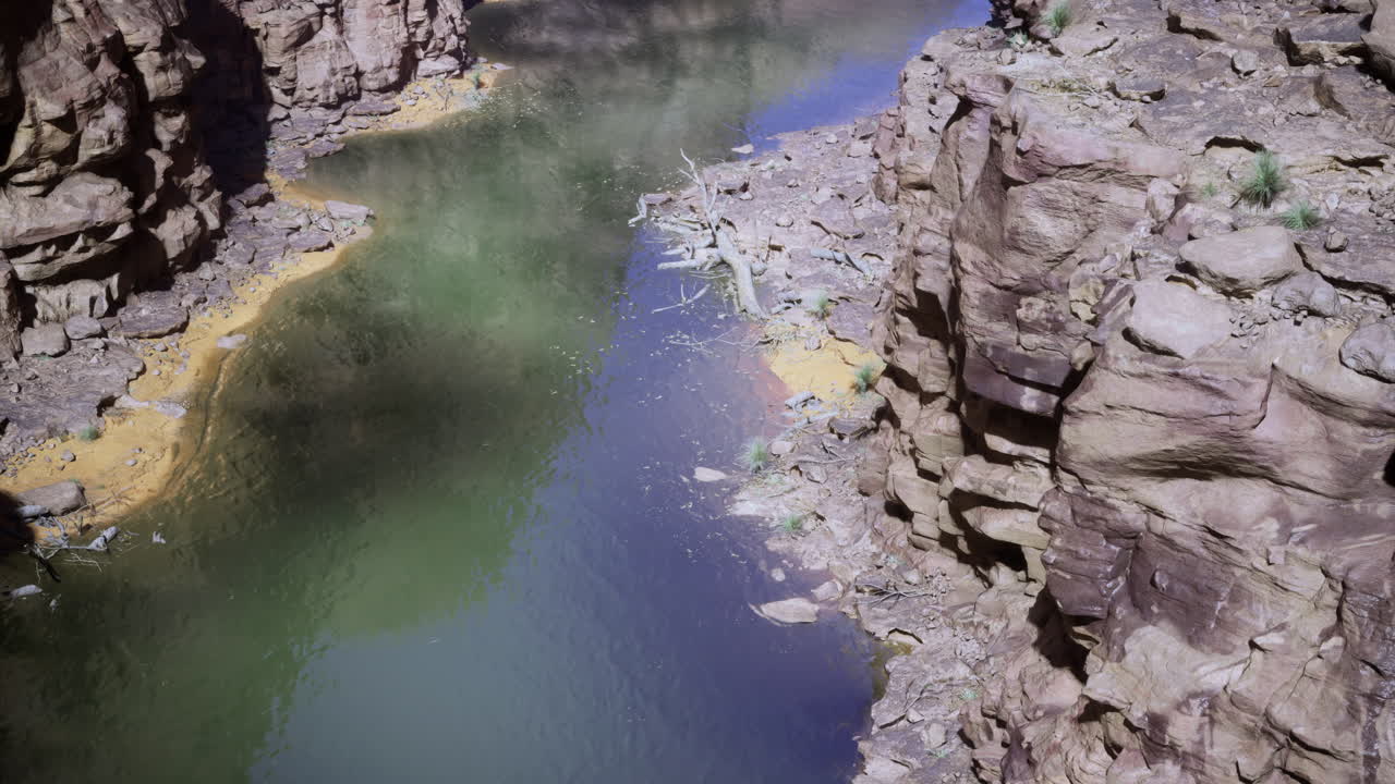 Rugged natural landscape with river beneath steep rock formations in sunlight