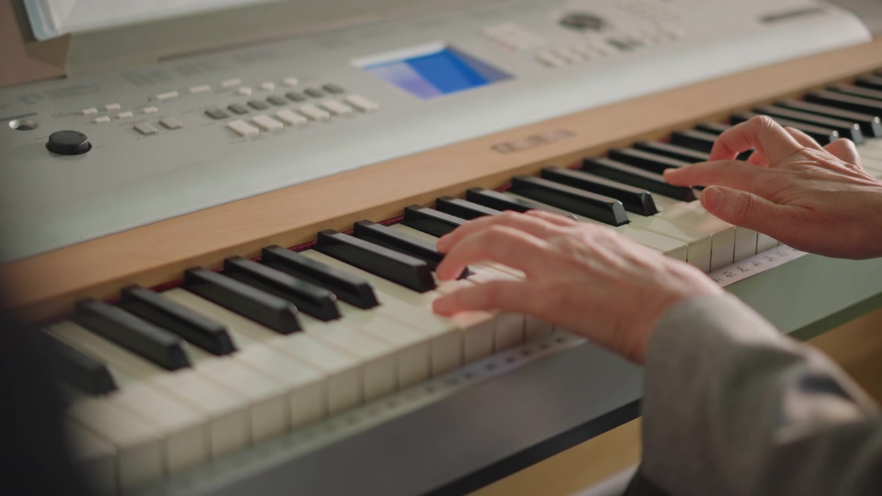 Primo piano delle mani di uno studente che pratica scale di pianoforte su tastiera digitale, display illuminato, osservazione paziente del tutor in primo piano, tempo costante, ripetizione diligente, atmosfera di lezione al chiuso.