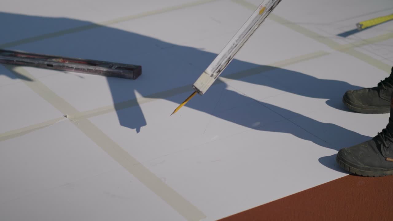 Close-up on a man drawing on taped paper sheets on the ground with a pencil. Scene from a construction site in Neot Smadar - Israel