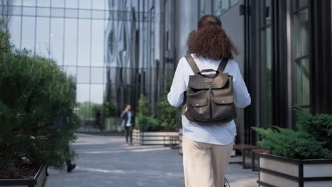 mujer de negocios relajada caminando por la calle del centro sosteniendo un scooter eléctrico vista trasera