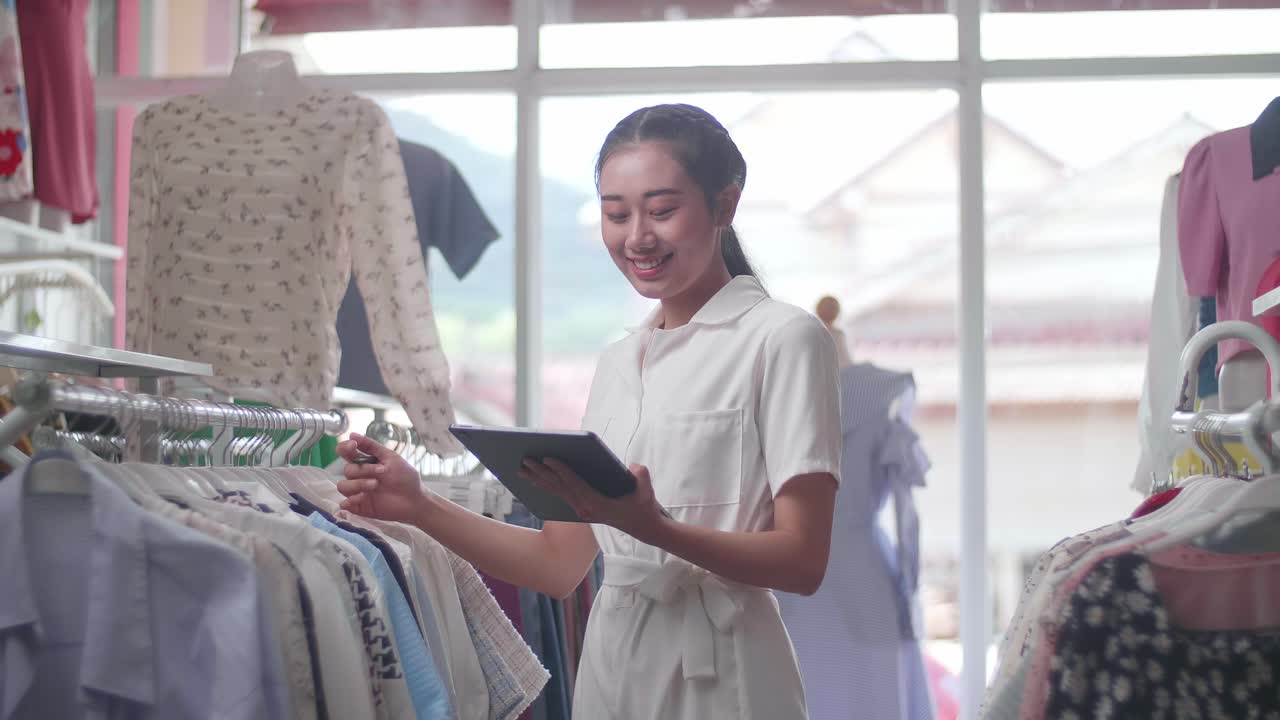 의류 가게의 아시아 여성 소유자는 디지털 태블릿을 사용하여 레일에 있는 재고를 확인하는 것을 즐긴다