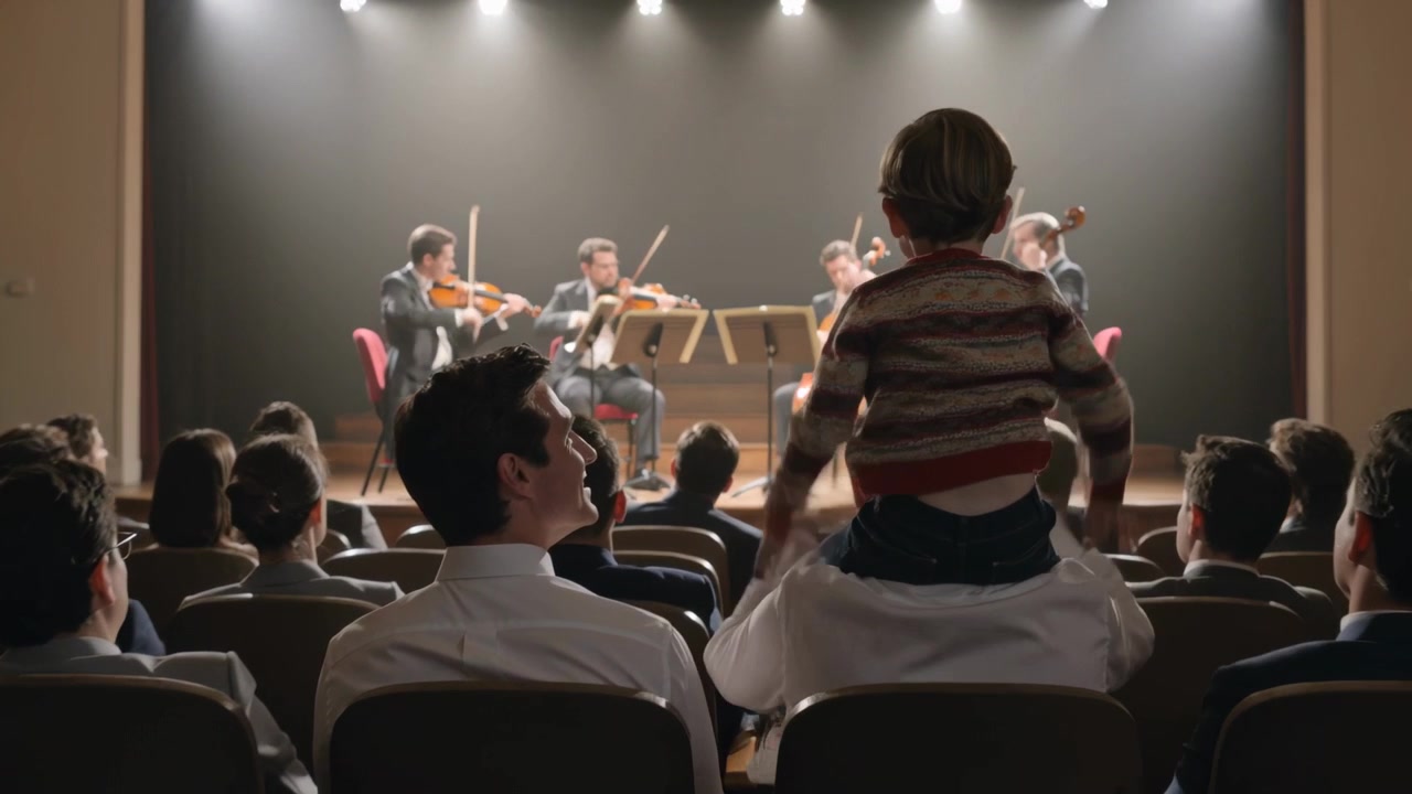 Uomo con camicia bianca solleva un bambino sulle spalle per fargli vedere uno spettacolo, mentre un quartetto suona.