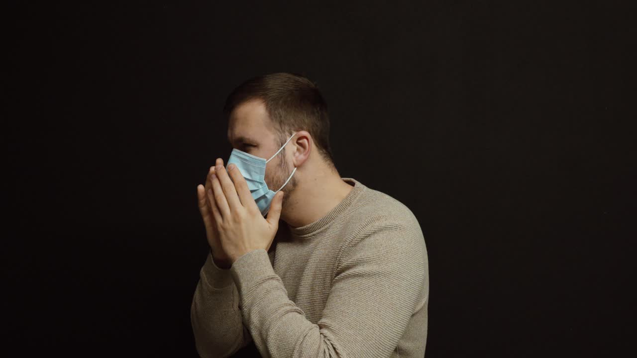 黒い背景に対し、防護マスクを着けて肘に咳をする男性。衛生、健康意識、病気の予防、責任ある行動の概念。