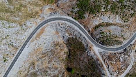 Drone-shot-of-a-car-driving-on-a-large-curvy-road-in-Andalusia,-Spain