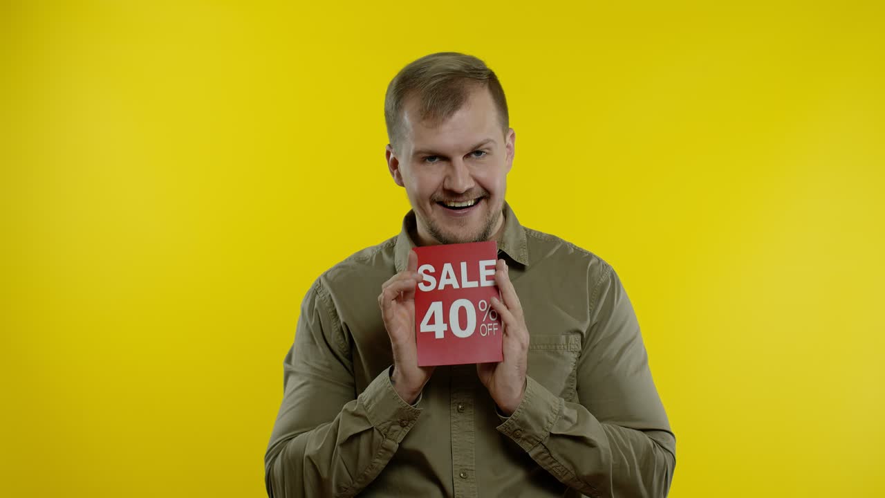 Uomo attraente che mostra cartelli con le scritte "Saldi 40% di sconto", rallegrandosi per i buoni sconti e i prezzi bassi.