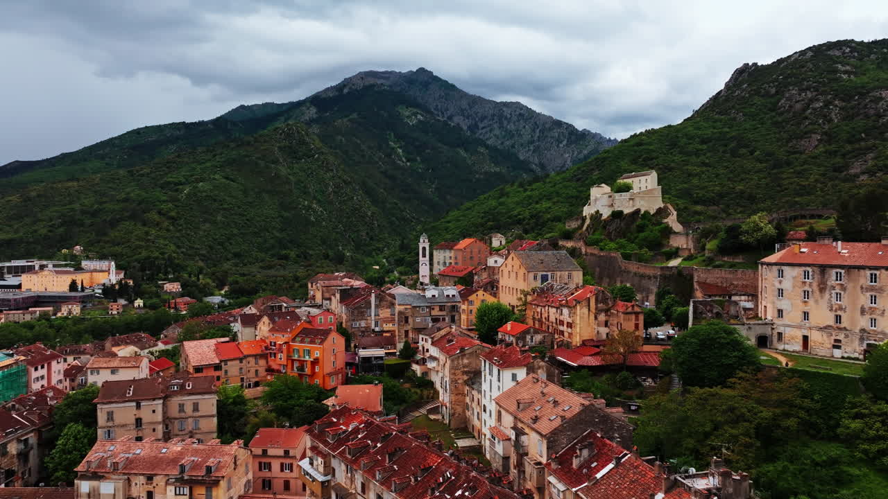 Aerial drone shot over the historic town of Corte, Corsica, France. High view of the old town and fortress overlooking the landmark on top of the hill. View of the scenic landscape and mountains
