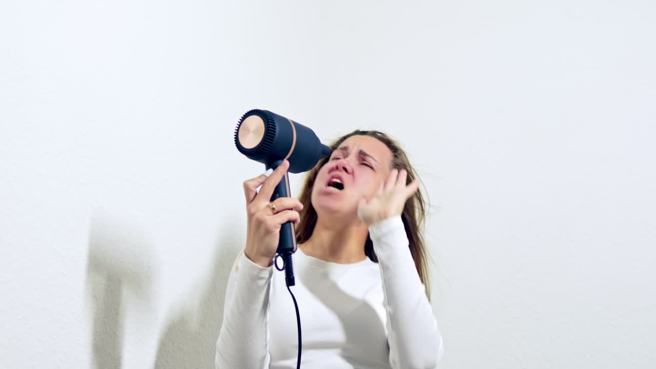 Donna che si asciuga i capelli con il phon e canta. Capelli belli e sani dopo trattamenti cosmetici. Bella donna sorridente che si pettina i lunghi e lucidi capelli con un pettine al mattino. Cura dei capelli.