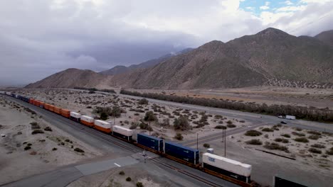 Aerial-Drone-Footage-of-Cargo-Train-in-Palm-Springs-Desert-with-Wind-Farms-in-the-Background,-slow-horizontal-moving-shot