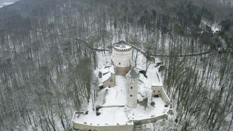 Drone-aerial-of-the-fairy-tale-castle-Plesse-in-winter-with-a-huge-amount-of-snow-on-a-beautiful-mountain-near-Bovenden,-Germany,-Europe