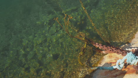 Looking-down-over-green-sea-water-with-a-large-rusty-chain-and-water-rippling