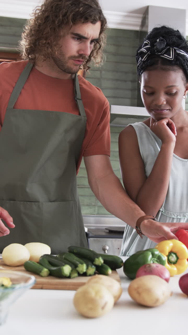 Vertical video: Diverse couple preparing vegetables in kitchen at home