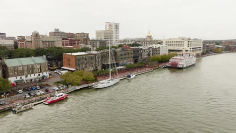 Drone-of-Savannah-Georgia-riverfront-area-along-the-river-approaching-boats-on-an-overcast-day