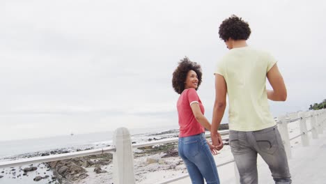 Afroamerikanisches-Junges-Paar-Hält-Händchen-Und-Umarmt-Sich,-Während-Es-Gemeinsam-Auf-Der-Promenade-Spaziert