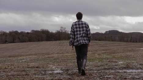 man in shirt and wellies walking through muddy countryside, graded slow motion