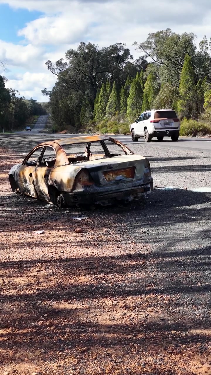 Inquadratura statica di un relitto di berlina carbonizzato accanto a una strada nella boscaglia nella foresta di Goonoo, Australia