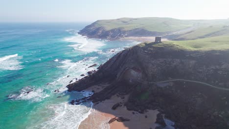 epic-aerial-of-mountain-sea-landscape-of-Spain,-Playa-de-Tagle,-panoramic-right-to-left-movement-of-a-landmark,-castle-watchtower-on-a-cliff