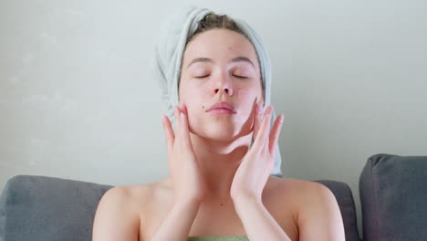 close-up of woman massaging skincare on her face with hands, focused on rejuvenating self-care routine, she is wearing a towel, enjoying a relaxing moment with a calming facial treatment