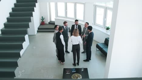 several intercultural business partners standing in circle inside office and listening to mature head of company giving them instructions