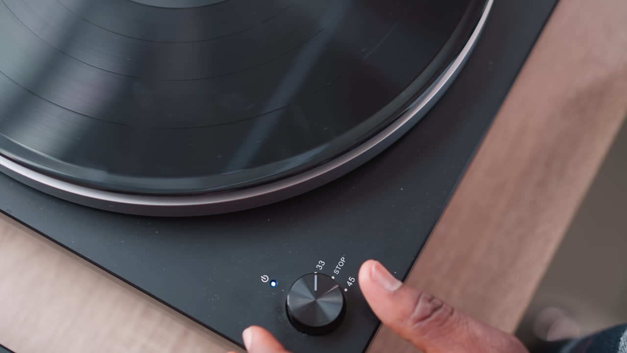 Hand of man activates switch on turntable. African American music lover entertains visitors immersed in favorite tunes through turntable. Music background