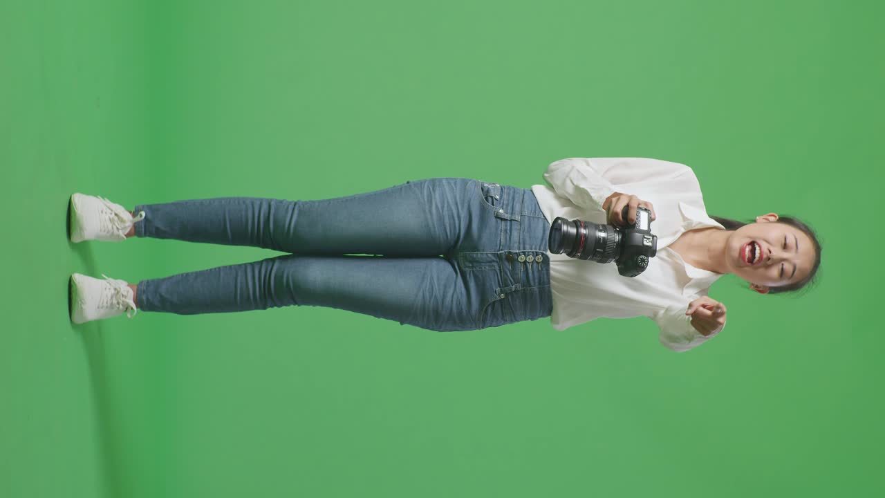 화가 난 아시아 사진작가의 몸이 가득 차 있습니다. 카메라를 사용해서 사진을 찍고 스튜디오에서 녹색 스크린 배경에 서서 누군가에게 소리치고 있습니다.