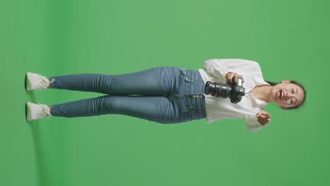 cuerpo lleno de fotógrafo asiático enojado usando una cámara tomando fotos y luego gritando a alguien mientras estaba de pie en el fondo de la pantalla verde en el estudio