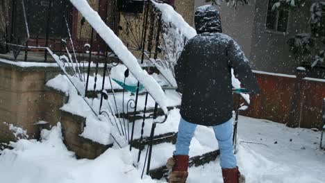 man sweeping snow from stairs near house in winter